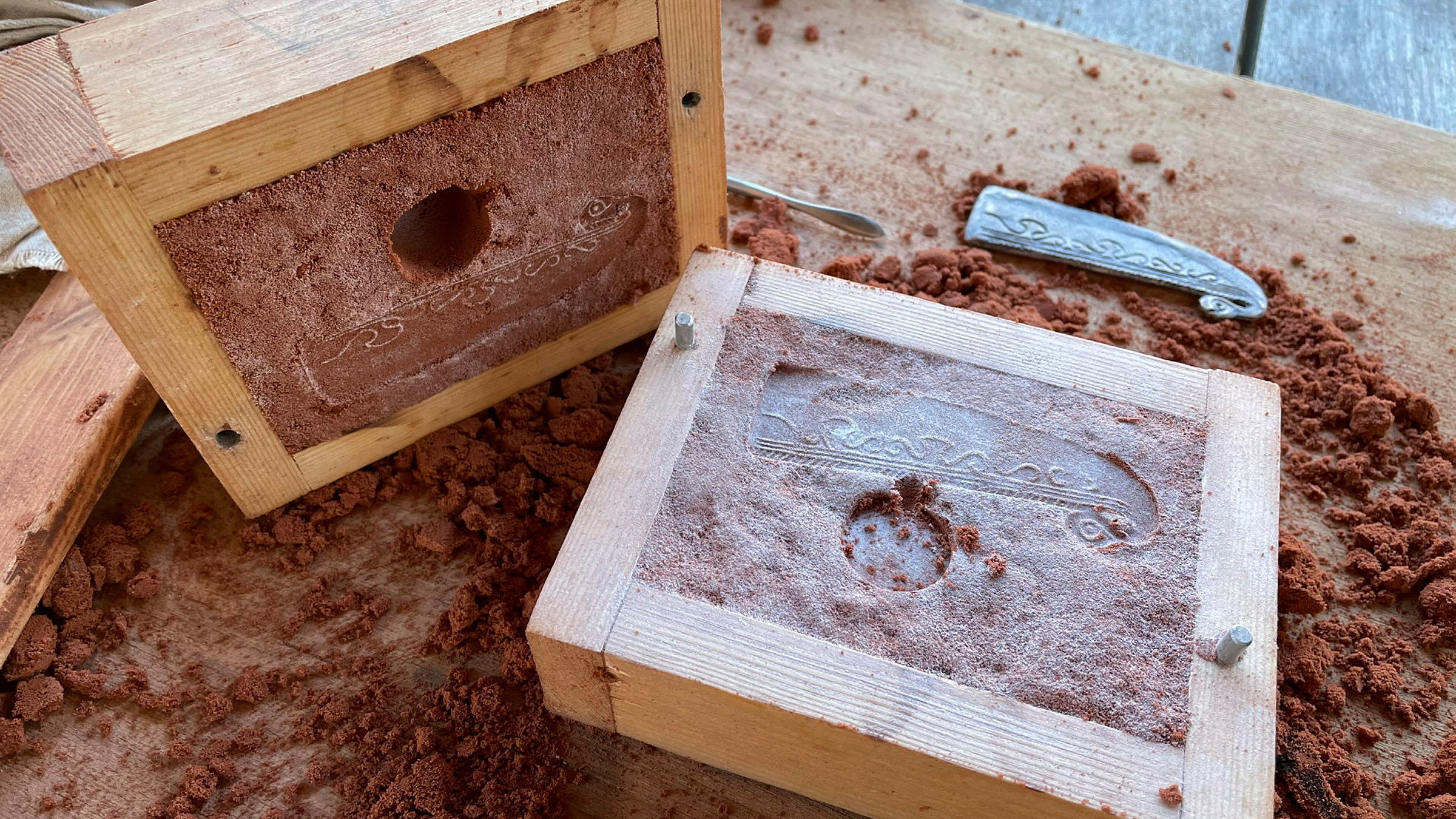 Formar fyllda med röd sand och ett avtryck av ett sirligt utsmyckat bronsåldersföremål i sanden