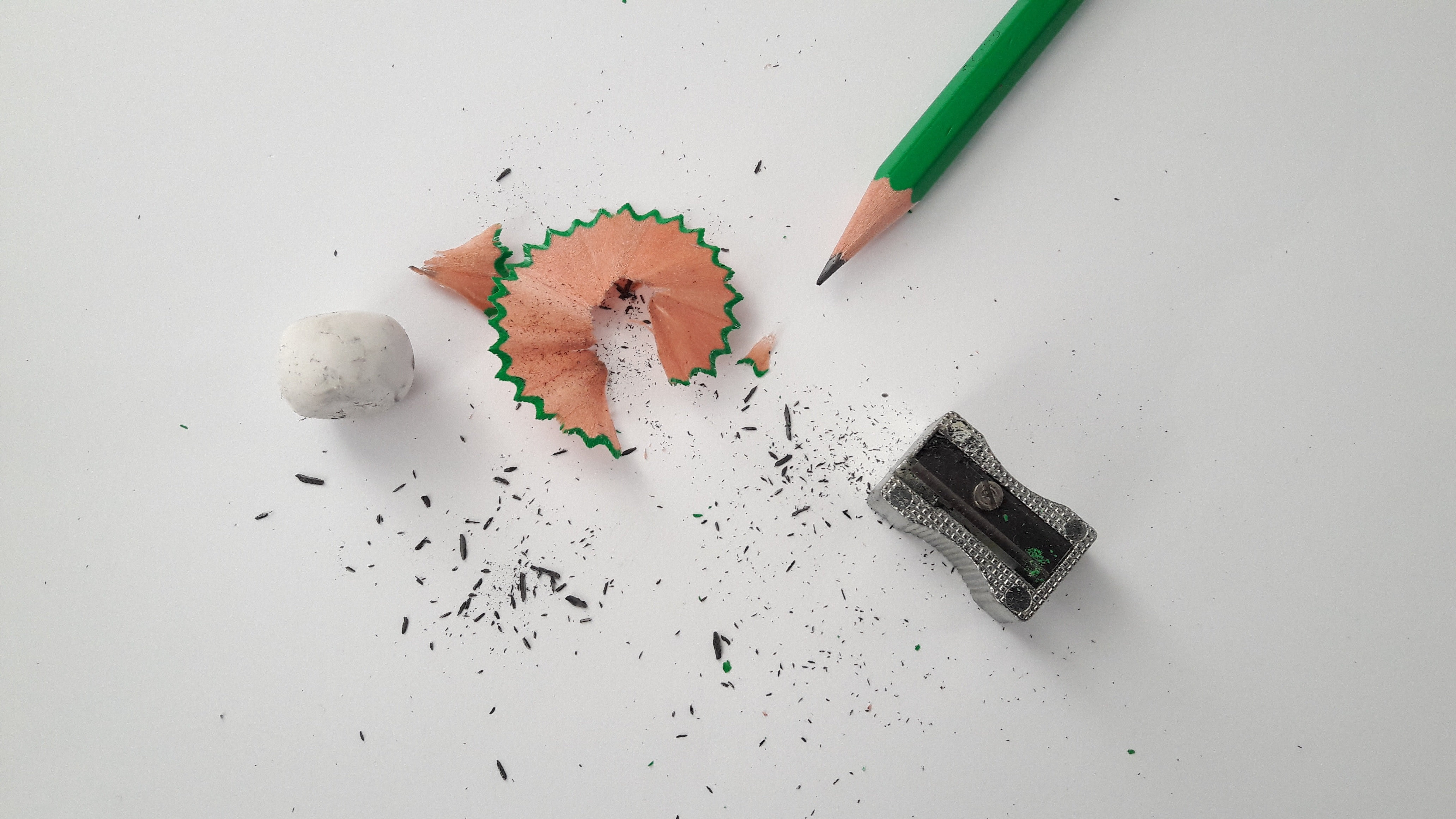 penna som vässats med pennvässare, radergummi och skräpet från vässandet mot vit bakgrund